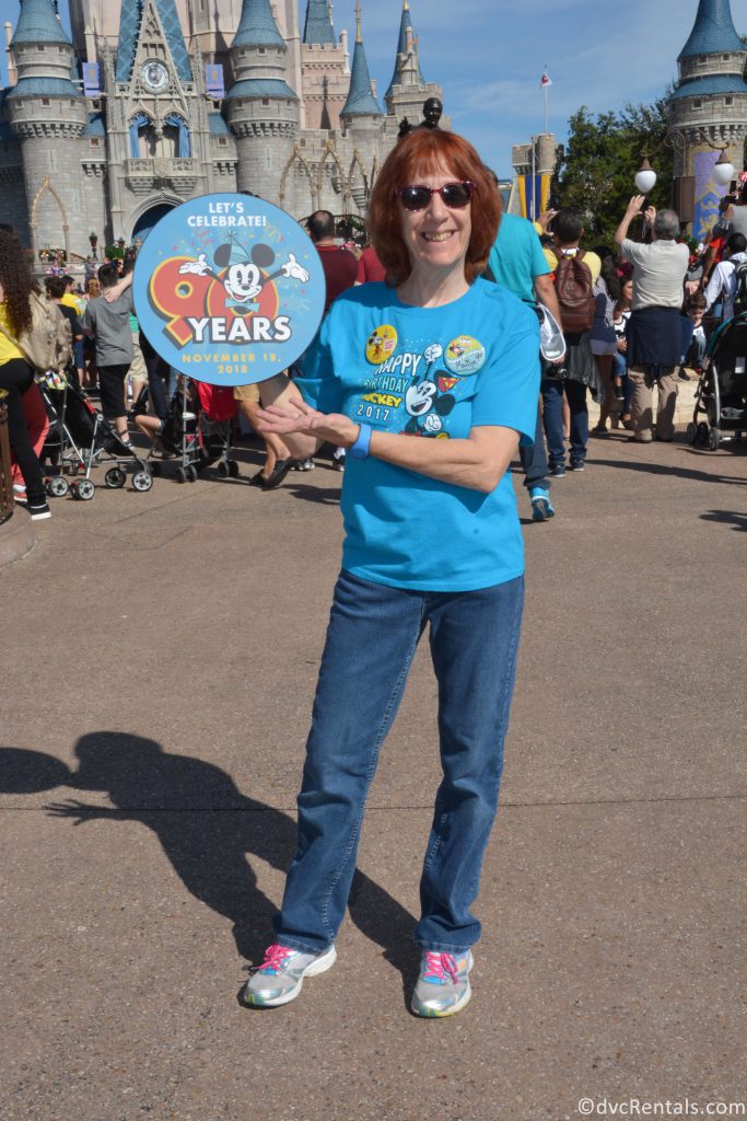 Marilyn standing in front of Cinderella’s Castle holding a Happy Birthday Mickey sign