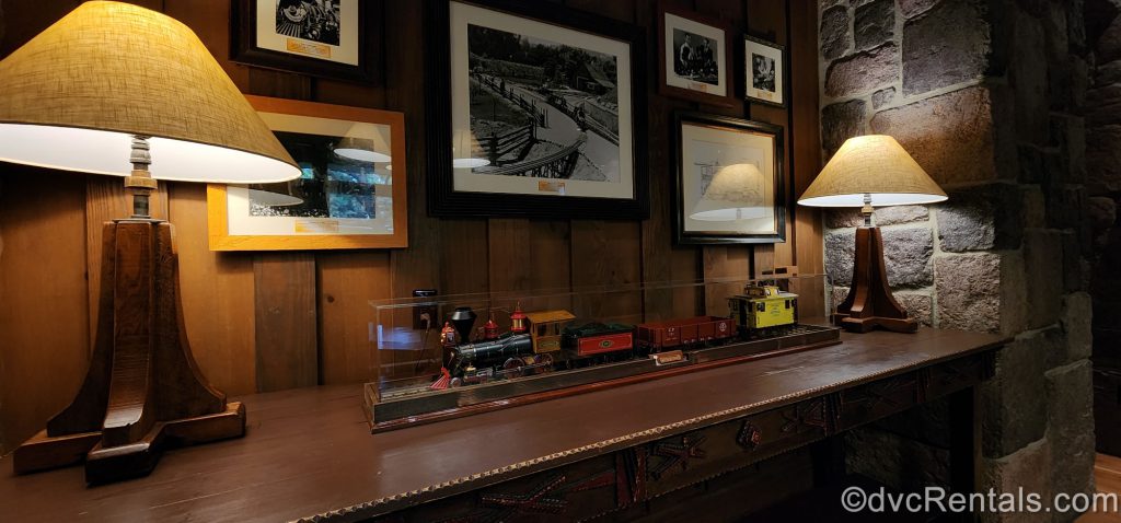 Model Train in a Case on a Wooden Table with Two Lamps and Photos of Trains on the Wall