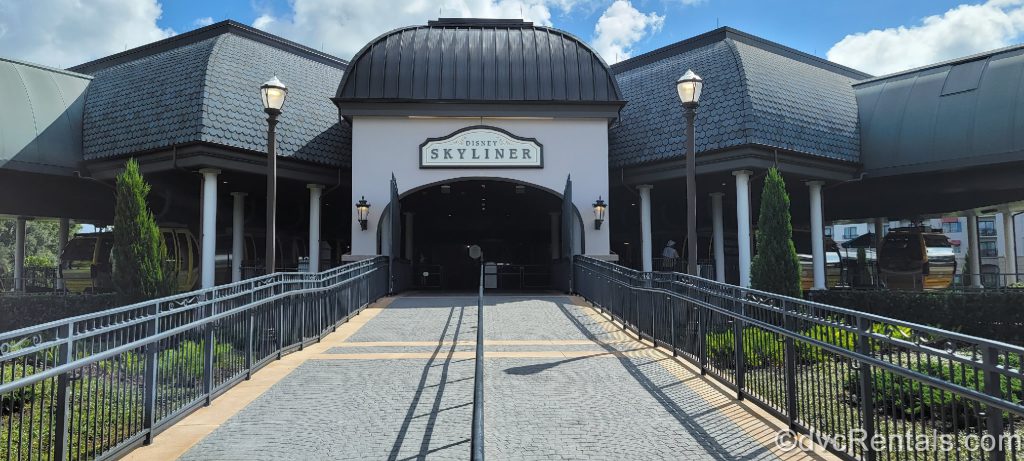 Disney Skyliner Hub Entrance. The hub is a dark gray building with a black roof. There are black railings leading up to the entrance, and the sign on the building reads, “Disney Skyliner.”