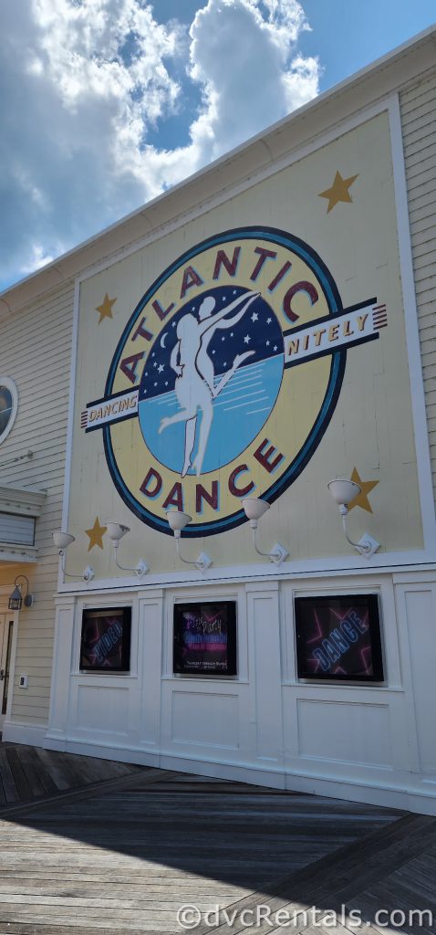 Pale yellow building with a yellow and blue sign that reads “Atlantic Dance Hall.” There is a painting of two people dancing within the words on the sign.