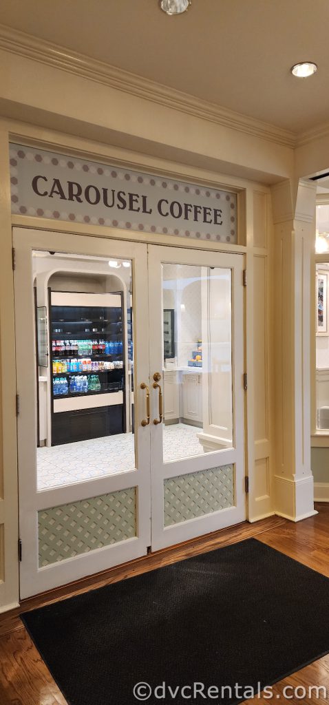 Glass door with white trim. Through the glass, a case full of cold drinks can be seen. The sign reads “Carousel Coffee.”