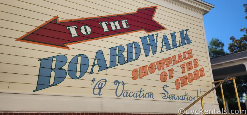 A sign painted on the side of the pale yellow building reads “To the Boardwalk. Showplace of the Shore. A Vacation Sensation.”