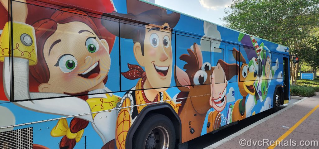 Photo 2: Bus stopped next to a curb. The bus is covered in characters from the movie Toy Story: Woody, Buzz Lightyear, Jessie, Bullseye, and Slinky Dog