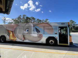 Bus stopped next to a curb. There is a picture of Dumbo flying on the bus, and the illuminated bus name says “Fort Wilderness”