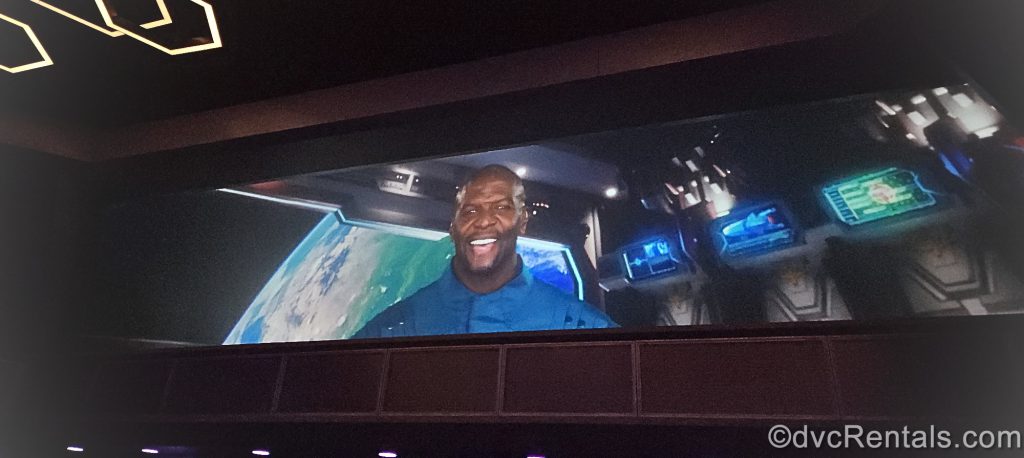 Snap of a video from the ride. The video is projected on the wall above everyone’s heads. Actor Terry Crews is on a spaceship with the Earth behind him.