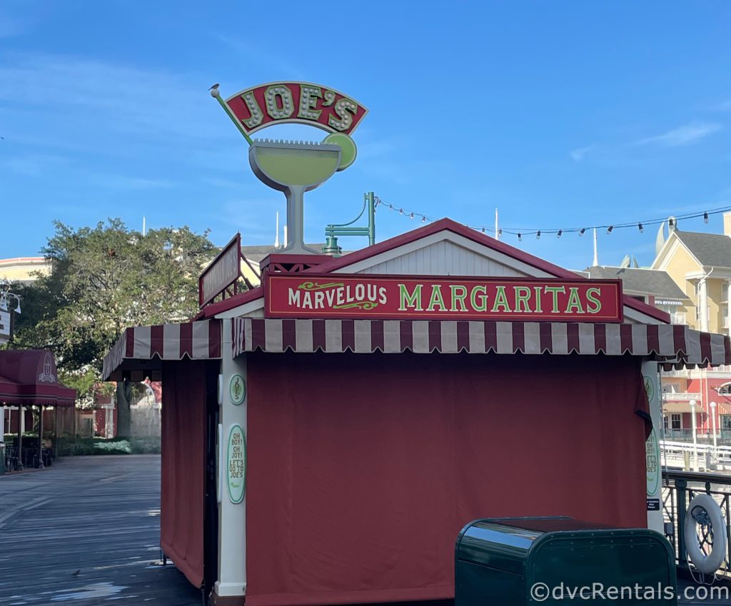 Boardwalk Joe’s Marvelous Margaritas Kiosk. The red and white hut is covered up with red curtains as it is closed. The red and green sign up top reads “Marvelous Margaritas,” and there is a cut out of a Margarita.