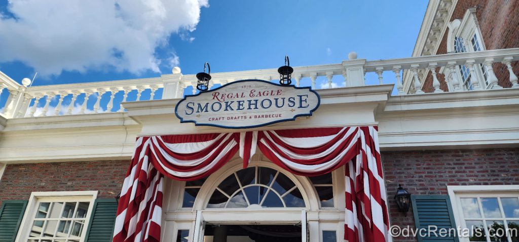 Regal Eagle Smokehouse Entrance. The red brick building has a white balcony and white trim around it, and an American Flag draped under the sign.