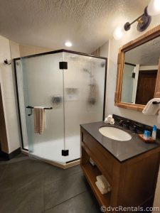 Stand-up shower with frosted glass and black trim. A wooden vanity with a white sink sits next to the shower. There is a mirror mounted over the vanity.