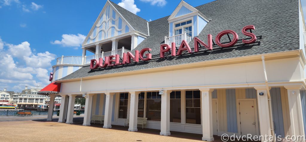 White and Light blue building with the sign “Dueling Pianos” in pink letters.