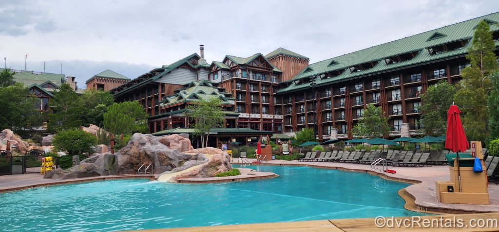 Copper Creek Springs Pool at Disney’s Wilderness Lodge. The log cabin-esque building with green accents can be seen in the background of the photo. A waterslide surrounded by fake rocks flows into the pool.