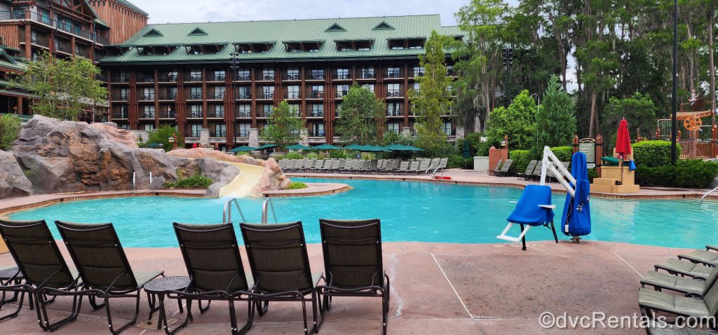 Copper Creek Springs Pool at Disney’s Wilderness Lodge. You can see the waterslide and the wheelchair-accessible water chair around the pool. On the pool deck are green lounger chairs and green umbrellas.