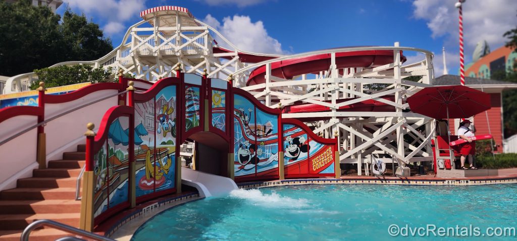 Keister Coaster waterslide at Luna Park Pool at Disney’s Boardwalk Resort. The waterslide is designed to look like a red-and-white rollercoaster track. A mural of Mickey Mouse, Minnie Mouse, Goofy, Donald, and Pluto sits on the pool deck and surrounds the slide exit into the pool.