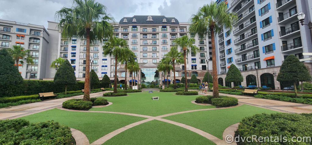 Disney’s Riviera Resort. There are two rows of palm trees lining the walkway towards the door.