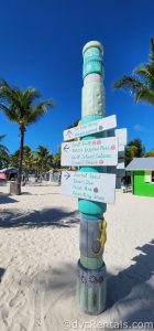 Post on the beach with directions signs pointing to landmarks on CoCo Cay.