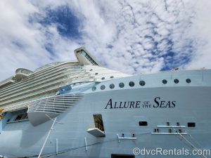 Royal Caribbean’s Allure of the Seas ship docked with a cloudy sky overhead.