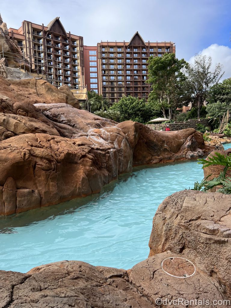 Lazy River surrounded by high rocks with the Aulani building in the background.