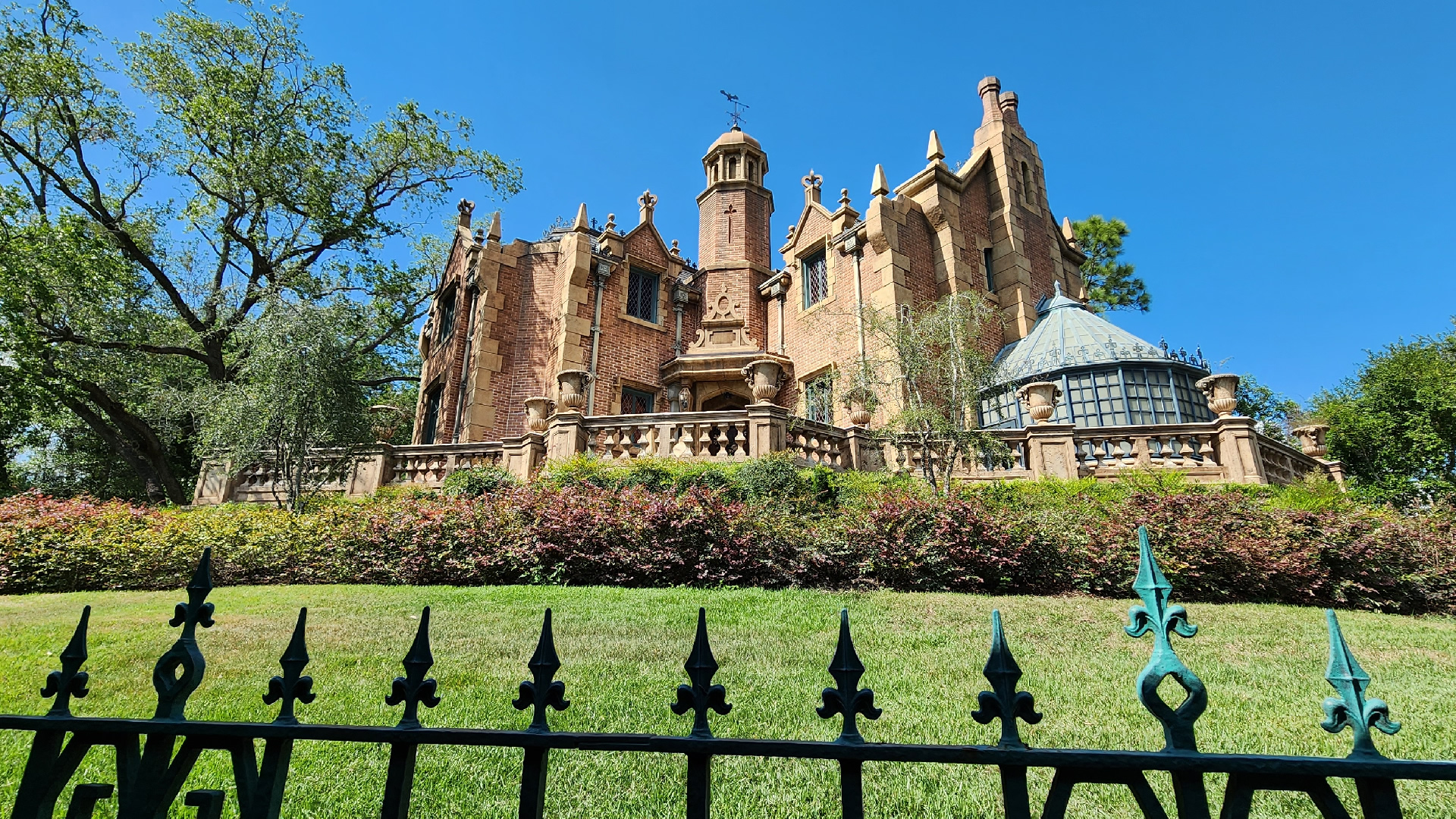 Haunted Mansion building, with green lawn, bushes, and an iron fence.