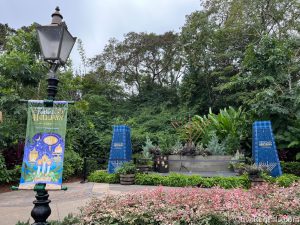 International Festival of the Holidays sign hanging from a lamp post with two stand-up signs sitting in a garden.