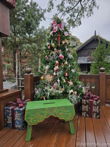Christmas Tree with Presents underneath and a green stool sitting on a wooden deck.