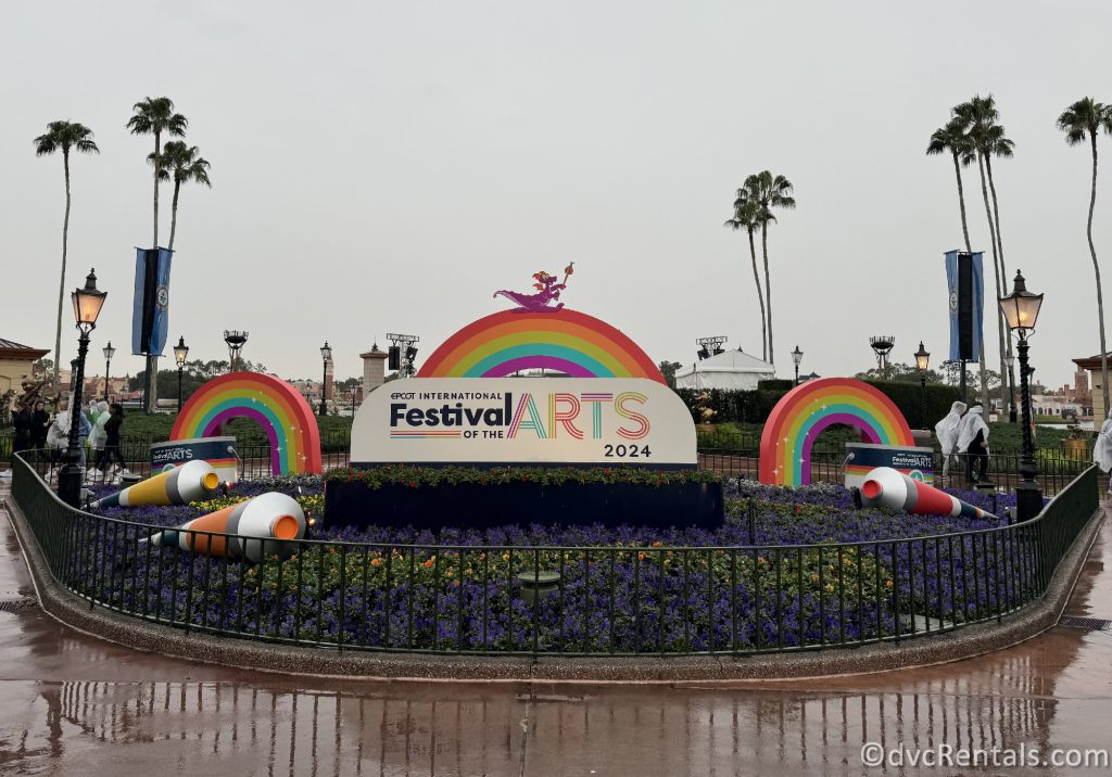 Festival of the Arts sign at the entrance to the World Showcase. Statues of rainbows, paints, and figures surround the sign.