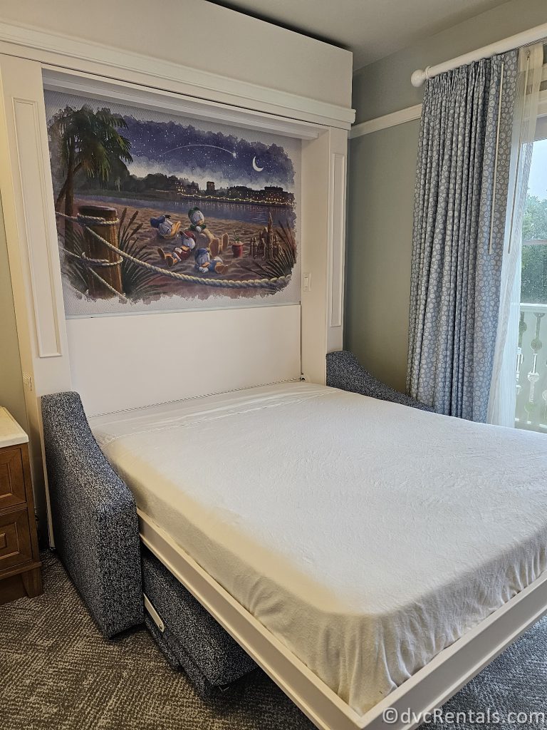 Pull-down bed in the Beach Club Studio. With the bed pulled down, there is a painting showing Donald Duck, Huey, Dewey, and Louie sleeping on the beach.