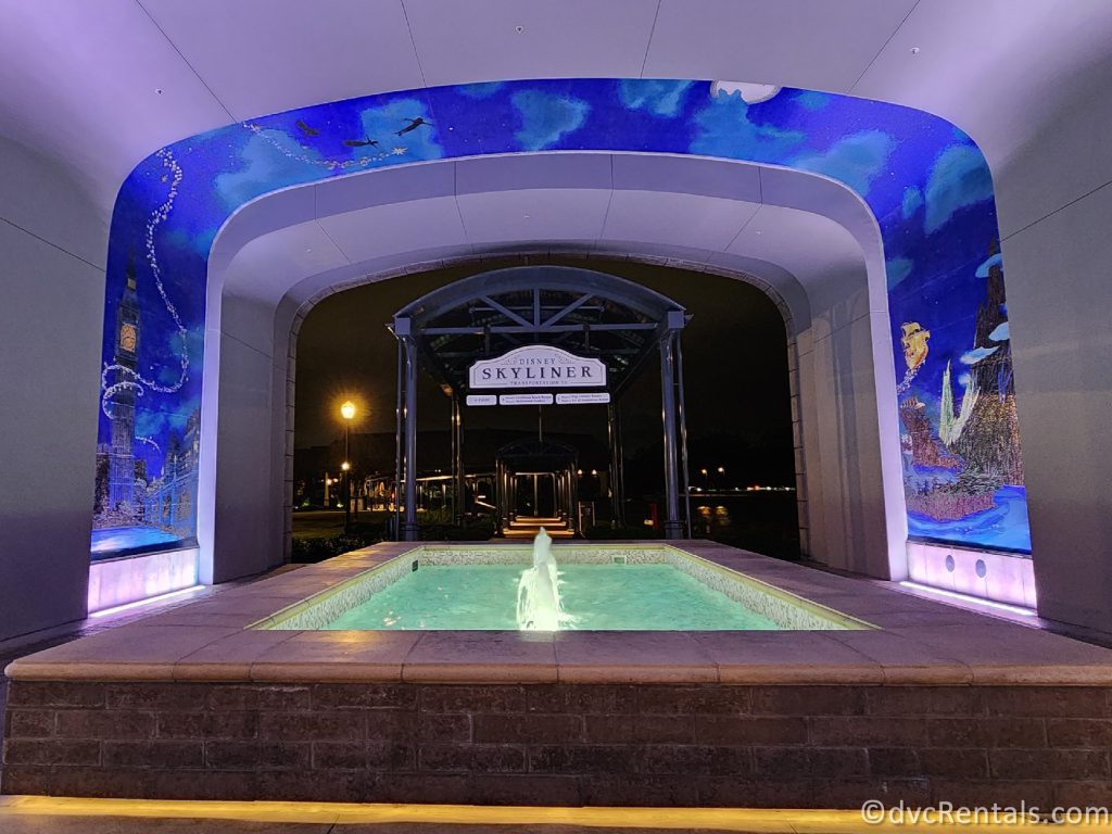 Fountain in the walkway lit up at night with the Peter Pan Mural and the Skyliner in the background.