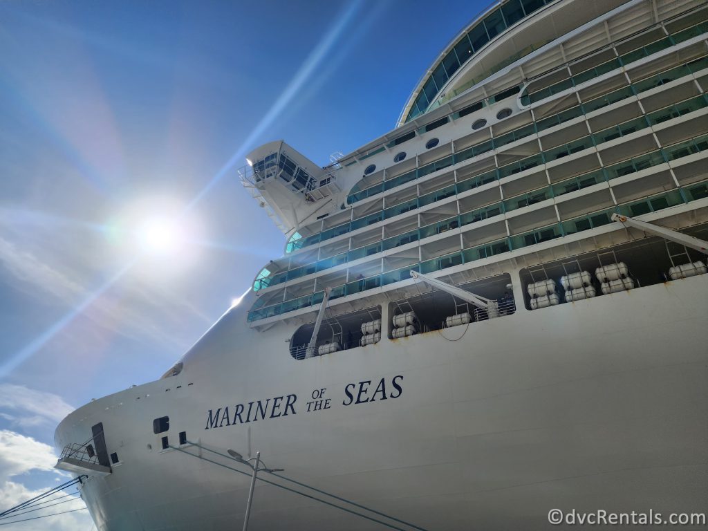 Front of Royal Caribbean's Mariner of the Seas ship docked at port. The white ship has the words "Mariner of the Seas" painted in blue on the side.
