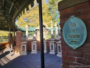 Queue for the Haunted Mansion in Magic Kingdom. A sign that reads "Open for Visitation" is on a brick wall, pointing toward five busts.
