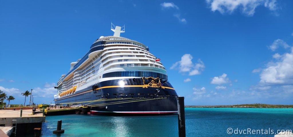 Disney Cruise Line's Disney Wish docked at Castaway Cay. The sky is blue above the ship, and the ocean is bright blue.