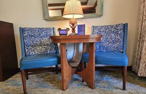 Two blue fabric chairs sitting on either side of a wooden table in the Studio at Disney's Polynesian Villas. There is a wooden lamp on the table that has a base shaped like the Tiki Statue from the Polynesian lobby.