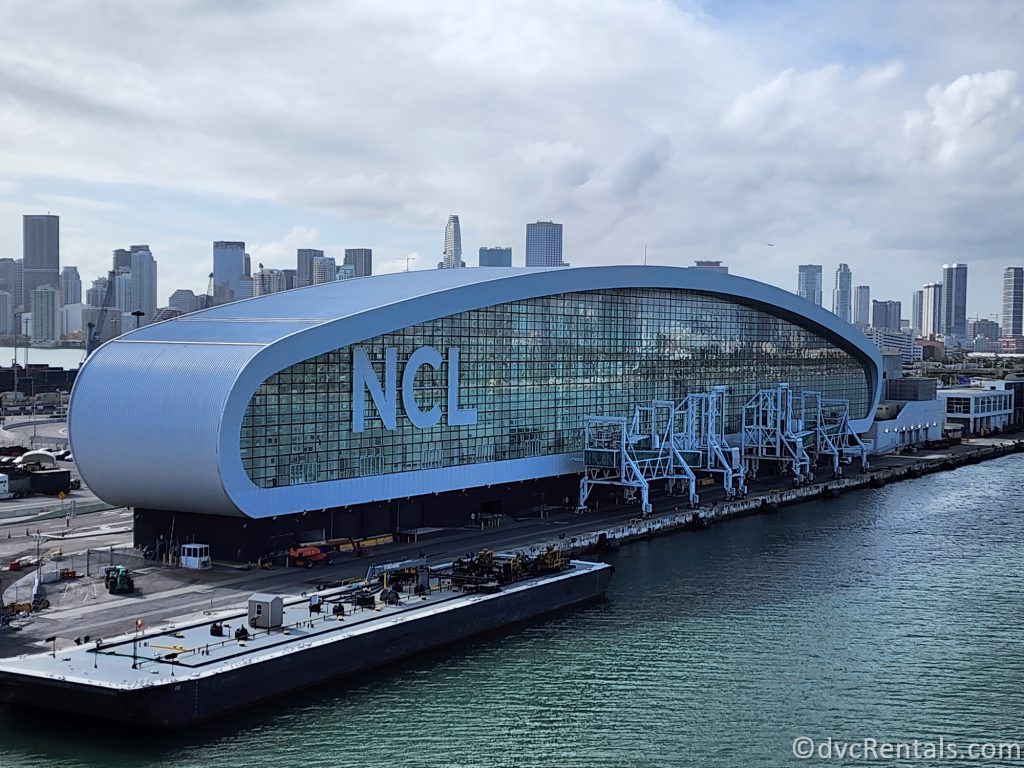 Norwegian Cruise Line's Cruise terminal in Miami. The large oval-shaped glass building has the letters "NCL" on the side of the building.