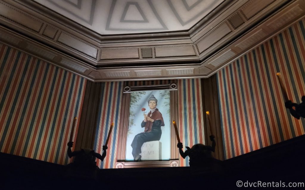 Painting of an older woman sitting on a tombstone in the stretching room on the Haunted Mansion.