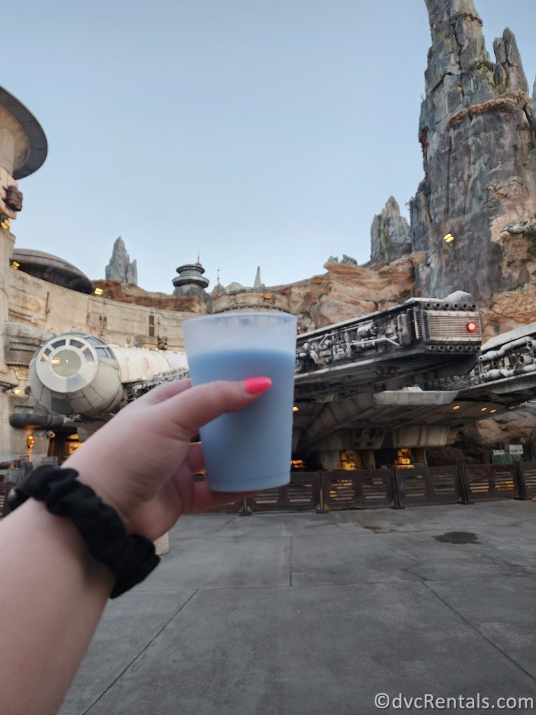 Blue Milk in a clear cup being held up in front of the Millennium Falcon in Star Wars: Galaxy's Edge at Disney's Hollywood Studios.