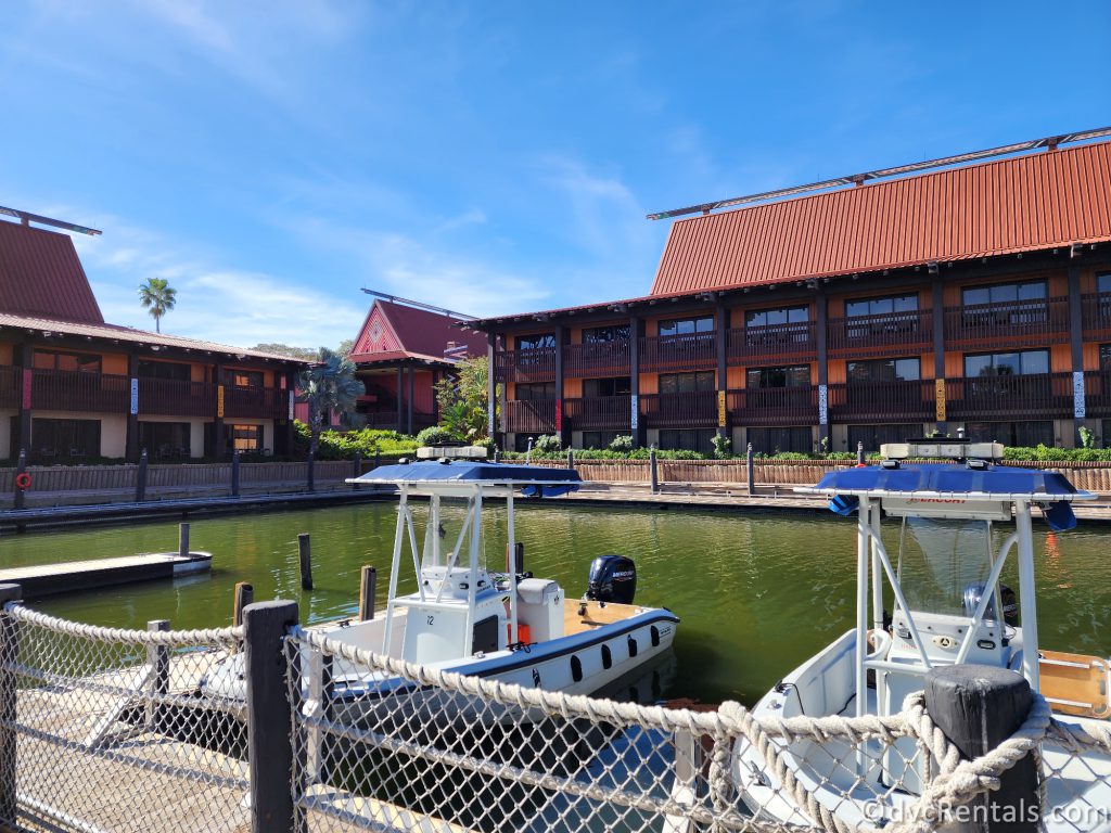 Boat dock at Disney's Polynesian Village Resort. Two boats are sitting in the water, and there are several dark wood buildings in the background.