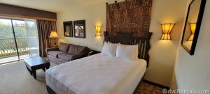 Main room in the Studio at Disney's Animal Kingdom Villas, Jambo House. A queen-sized bed with an ornate wooden headboard sits next to a brown couch and dark wood coffee table.
