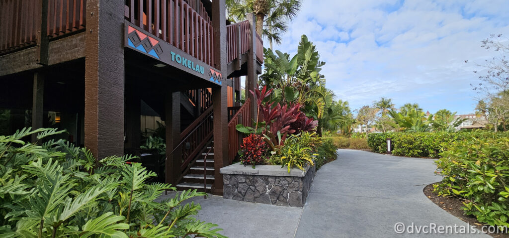 Entrance to the Tokelau building at Disney's Polynesian Villas. The dark wood building is nestled amongst many colorful plants and greenery.