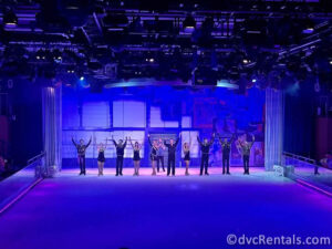 10 skaters in black outfits bowing on the ice rink.
