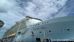 Allure of the Seas cruise ship docked in Nassau. There are bright blue skies above the ship with fluffy white clouds.