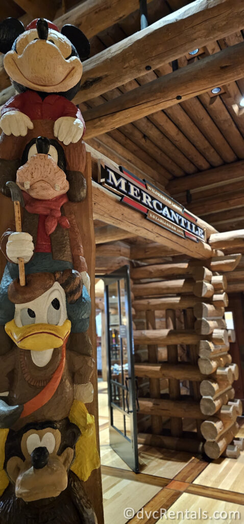 Exterior of Wilderness Lodge Mercantile at Disney's Wilderness Lodge. There is a wooden totem pole out front featuring Mickey Mouse, Goofy, Donald Duck, and a bear.