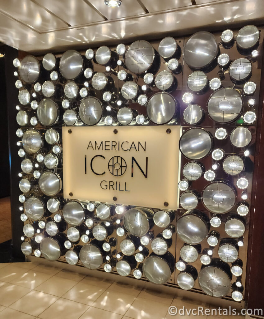 Sign for the Entrance to the American Icon portion of the Main Dining onboard Allure of the Seas. The white sign is surrounded by large silver balls.