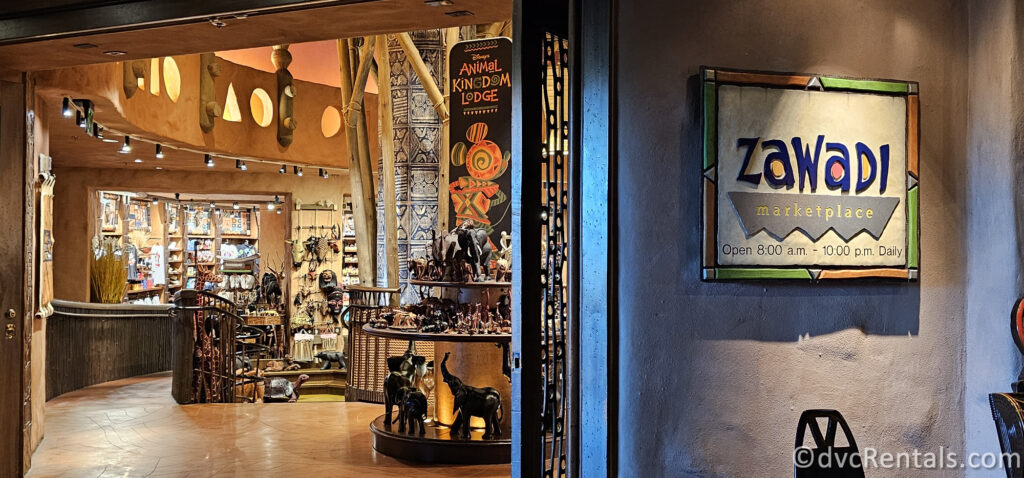 Exterior of Zawadi Marketplace at Disney's Animal Kingdom Villas - Jambo House. The sign for the store is to the right of the open entrance, and inside the store, you can see African-inspired souvenirs.