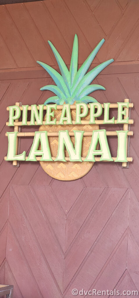 Pineapple Lanai Sign hanging on the wood wall at Disney's Polynesian Villas. The yellow letters that read "Pineapple Lanai" sit on top of a cut out of a Pineapple.