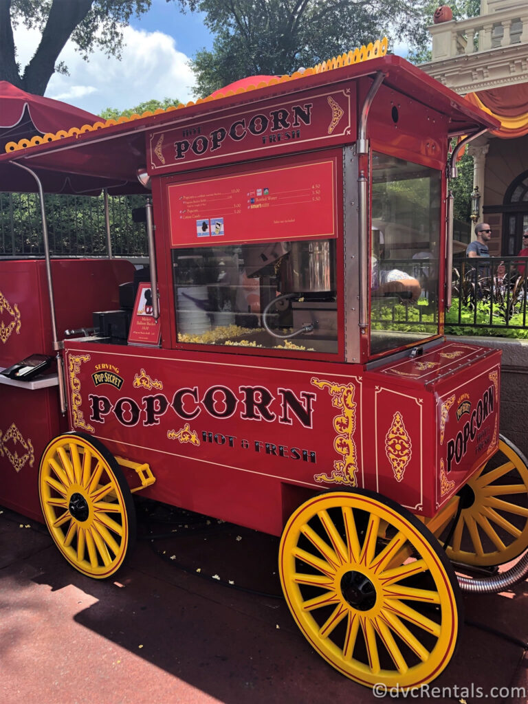 Red popcorn cart with bright yellow tires selling popcorn in Magic Kingdom.