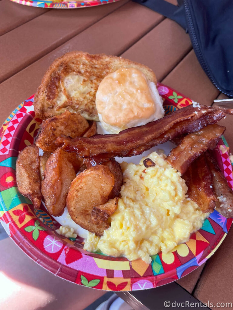 Bounty Breakfast Platter on a Disney-themed paper plate from Capt. Cook's. The Breakfast Bounty Platter includes scrambled eggs, bacon, sausage links, french toast, potatoes, and a biscuit.