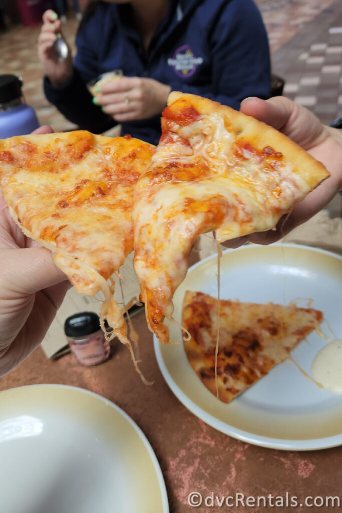 Two people doing cheers with two slices of cheese pizza from Sorrento's.