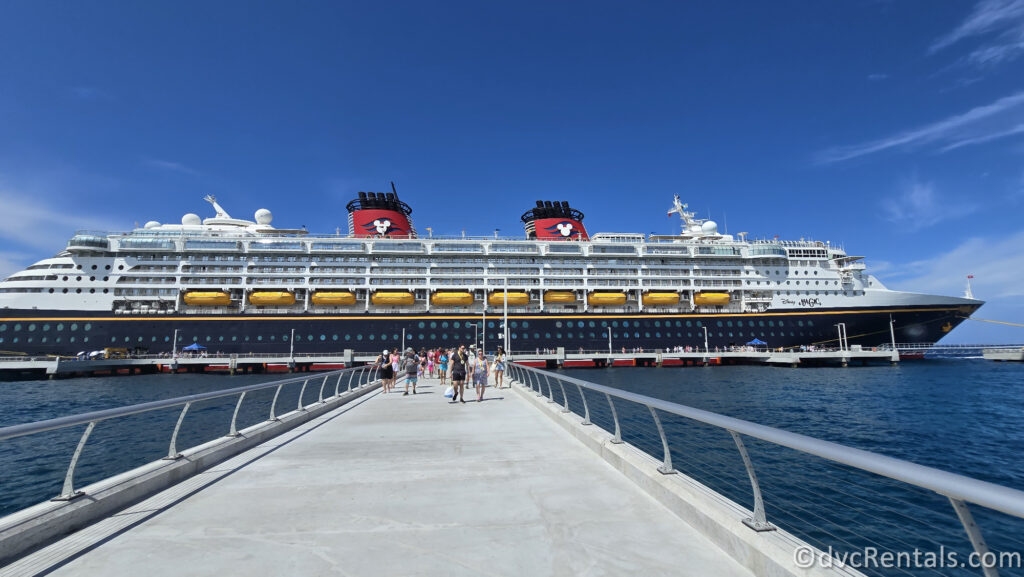 Disney Magic Cruise Ship docked at the pier at Lighthouse Point. There is a group of people in the distance walking down the pier.