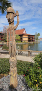 Wooden Tiki Statue standing in a garden with Disney's Polynesian Villas in the background.