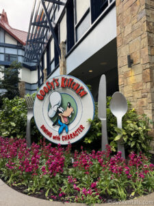 Sign for Goofy's Kitchen. The words reading "Goofy's Kitchen" are sitting upon a large metal sign shaped like a plate, with Goofy's face on it as well. There is also a metal fork, knife, and spoon next to the plate.