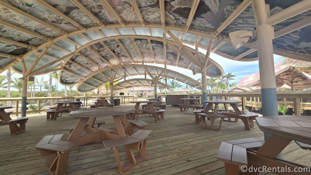 Wooden Picnic Tables sitting on a wooden deck covered by a large wooden canopy.