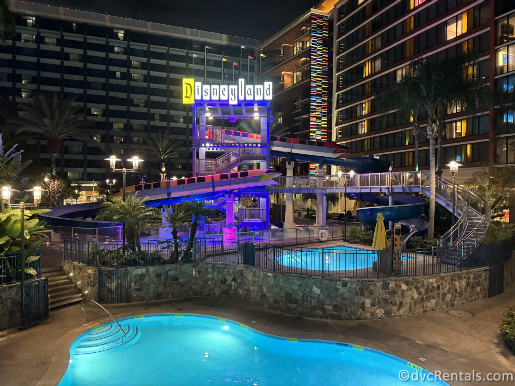 Disneyland Hotel Monorail pool at night. A large Disneyland sign shines with colorful lights upon the monorail statues above the pool.